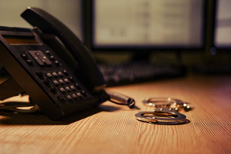 A business phone and handcuffs sit on a desk. This image visually supports legal content about false imprisonment or malicious prosecution.